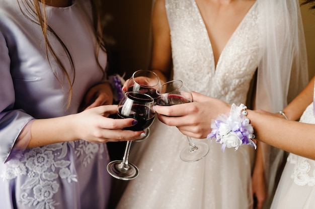 Superbe mariée et demoiselles d'honneur grillage avec du vin et s'amuser le matin du mariage. Mains tenant des verres élégants avec des boissons et des tintements.