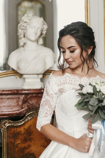 Photo superbe mariée en robe élégante avec un bouquet incroyable posant dans une chambre de luxe à l'hôtel belle femme tenant des fleurs et debout près du moment sensuel du monument