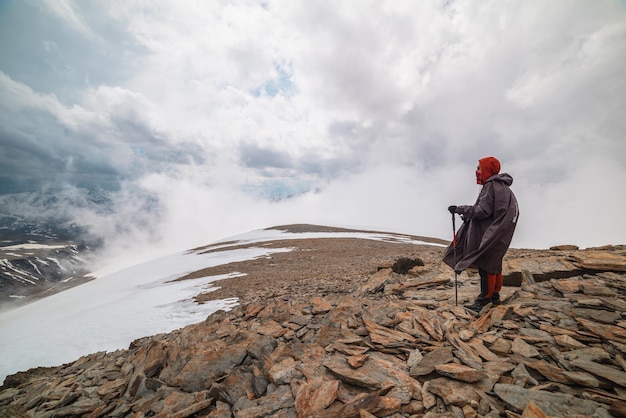 Superbe paysage de montagne minimaliste avec un randonneur à très haute altitude dans des nuages bas denses Magnifique paysage alpin avec un homme sur une colline de pierre avec de la neige dans des nuages épais Nature de l'homme et des montagnes majestueuses