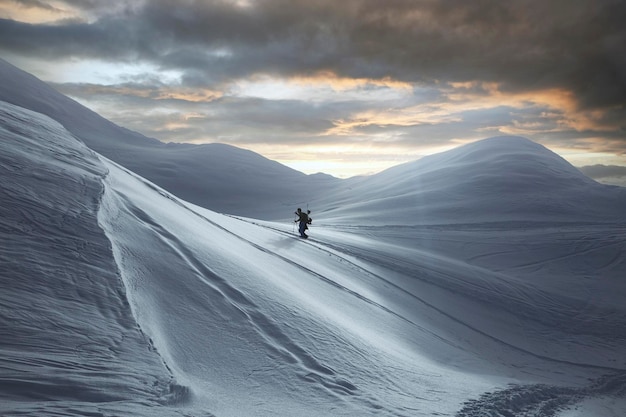 Superbe vue sur la haute chaîne de montagnes enneigées et le skieur marchant le long de celle-ci Nuages de brouillard et ciel coloré