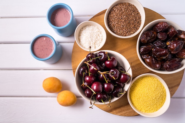 Superfoods dans des bols, des cerises fraîches et des smoothies, sur du bois blanc.