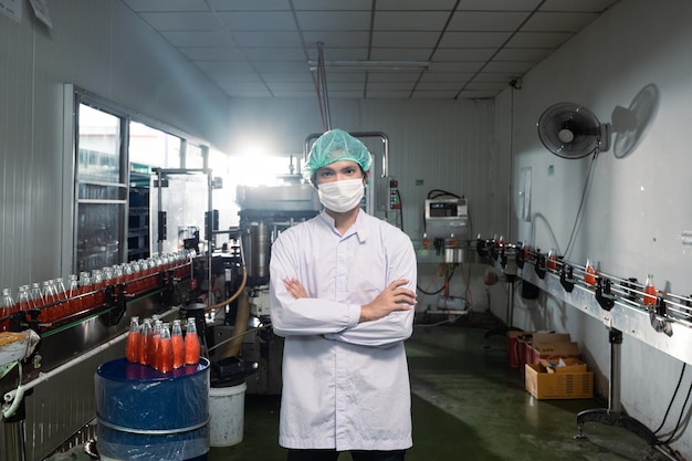 Superviseur asiatique homme en costume stérile debout avec une ligne de production en bouteille dans une usine de transformation de boissons