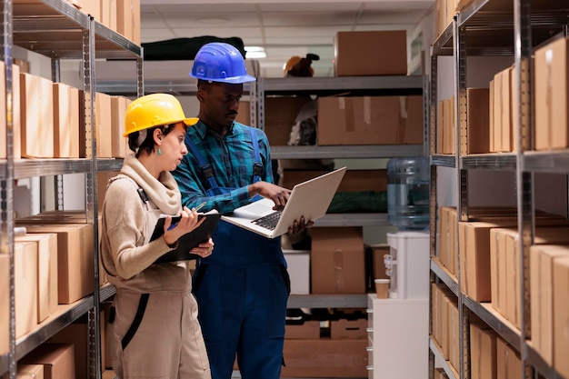 Les superviseurs d'entrepôt discutent de l'inventaire des marchandises et vérifient le rapport sur un ordinateur portable. Homme et femme divers collègues de l'entrepôt supervisant les opérations de réception et d'entretien du fret