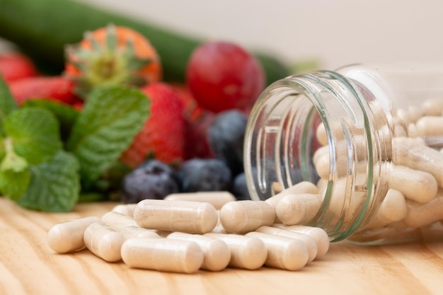 Photo suppléments de vitamines dans la bouteille en verre sur la table en bois avec des fruits variés