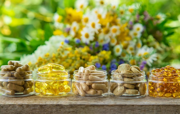 suppléments, vitamines et herbes médicinales dans des bocaux en verre sur table en bois sur fond de fleurs floues