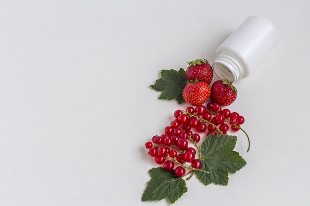 Suppléments de vitamines sous forme de capsule avec des baies fraîches provenant d'un flacon de pilules blanches médicinales.