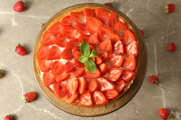 Support en bois avec tarte aux fraises sur fond texturé gris.