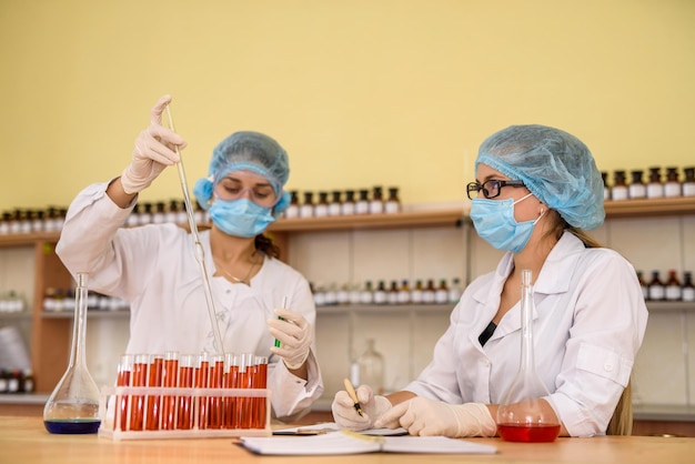 Support de chimiste avec des tubes à essai de couleur rouge et des mains humaines dans des gants de protection