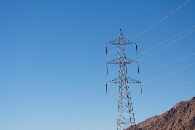 Support électrique des câbles d'alimentation haute tension. Support métallique avec isolateurs haute tension et contre le ciel bleu dans le désert avec collines et montagnes.