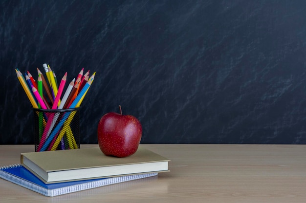 support métallique avec des crayons et une pomme rouge et des livres sur le bureau sur fond de tableau noir