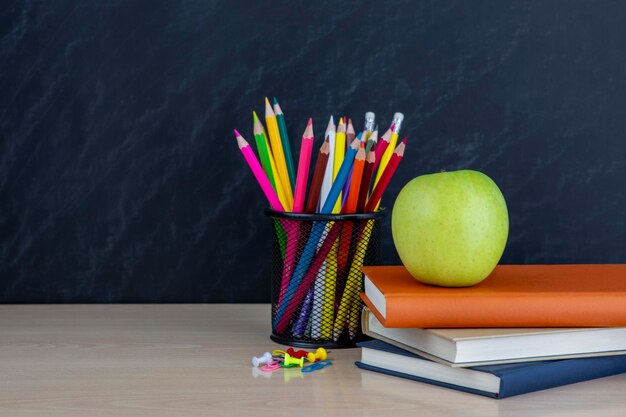 Photo support métallique avec des crayons et des pommes vertes et des livres sur le bureau sur fond de tableau noir