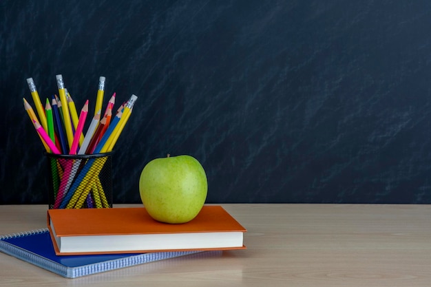 Photo support métallique avec des crayons et des pommes vertes et des livres sur le bureau sur fond de tableau noir