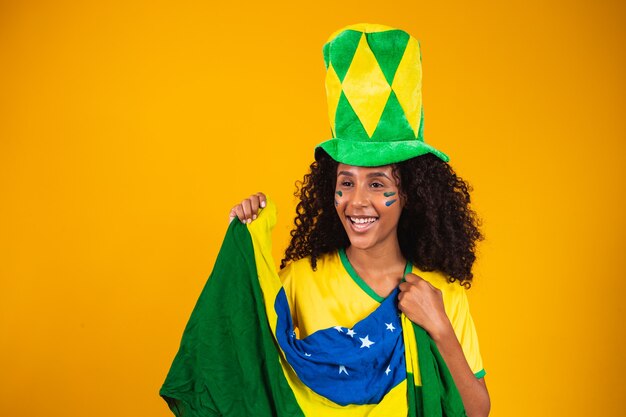 Supporter brésilien. Fan de femme brésilienne célébrant le match de football ou de football sur fond jaune. Couleurs du Brésil.