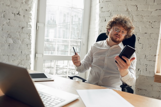 Surf, lecture. Caucasien jeune homme en tenue d'affaires travaillant au bureau. Jeune femme d'affaires, gestionnaire effectuant des tâches avec un smartphone, un ordinateur portable, une tablette a une conférence en ligne. Concept de travail, éducation.