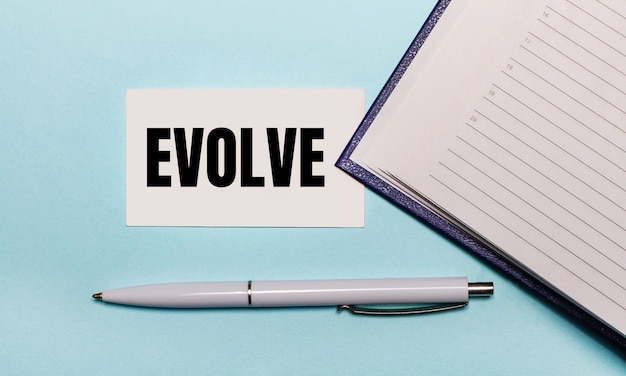 Sur une surface bleu clair, un cahier ouvert, un stylo blanc et une carte avec le texte EVOLVE