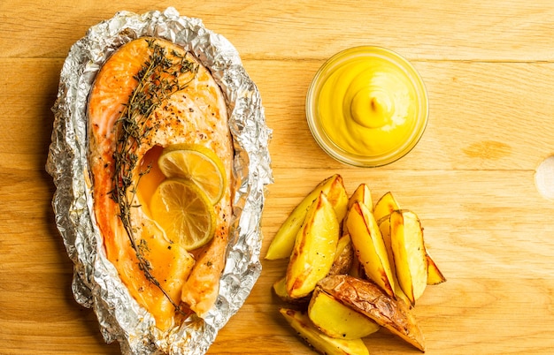 Surface en bois de la planche à découper et savoureuses pommes de terre frites avec de la moutarde dessus. Poisson frit en papillote près