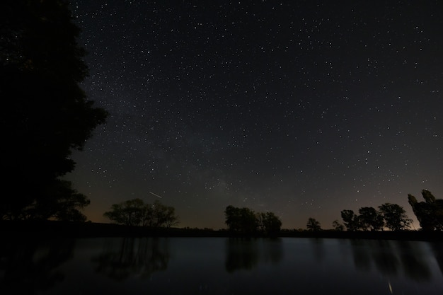 Surface lisse du lac forestier sur fond de ciel nocturne et de voie lactée.