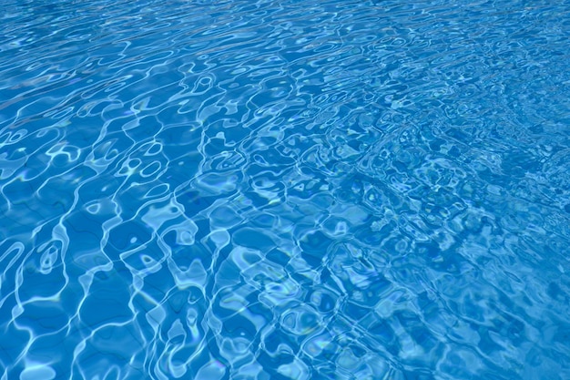 Surface ondulée de l'eau bleue au fond de la piscine