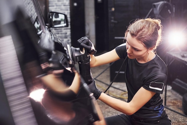 Surface de polissage du véhicule L'automobile noire moderne est nettoyée par une femme à l'intérieur de la station de lavage de voiture