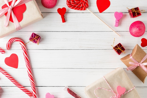Surface de la Saint-Valentin. Cadre de coeurs rouges, boîte-cadeau avec ruban et bonbons sur une surface en bois blanche, vue de dessus