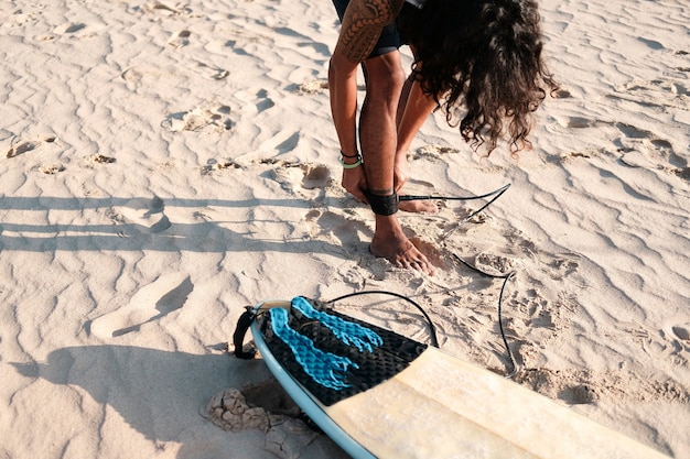 Surfer homme assis à la planche de surf sur la plage de sable