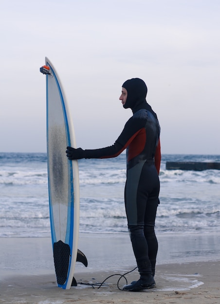 Surfer avec planche de surf debout. Il porte une combinaison