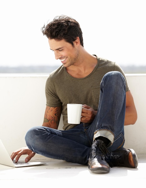 Surfer sur le Web à l'extérieur Un beau jeune homme assis dehors avec son café tout en utilisant son ordinateur portable