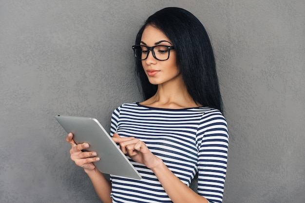 Surfer sur le Web sur sa nouvelle tablette. Gros plan sur une belle jeune femme africaine travaillant sur une tablette numérique en se tenant debout sur fond gris