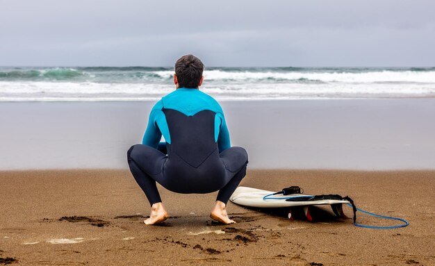 Photo surfeur assis devant la mer avec son espace de copie de planche