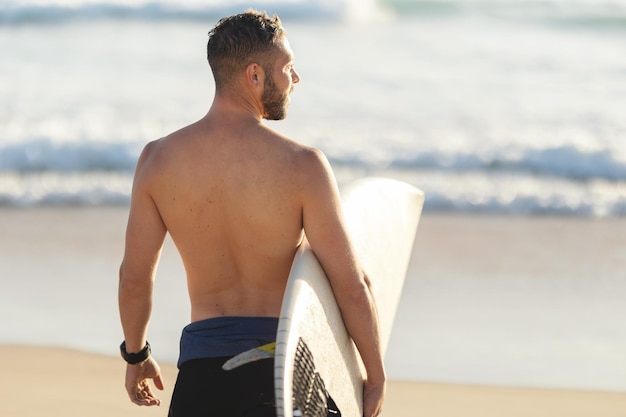 Un surfeur athlétique au torse nu debout au bord de l'océan