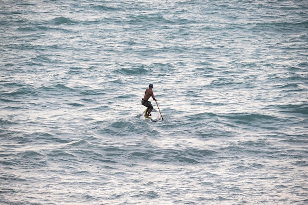 Un surfeur athlétique nage avec une pagaie sur une planche de surf dans la mer Stand up paddleboarding