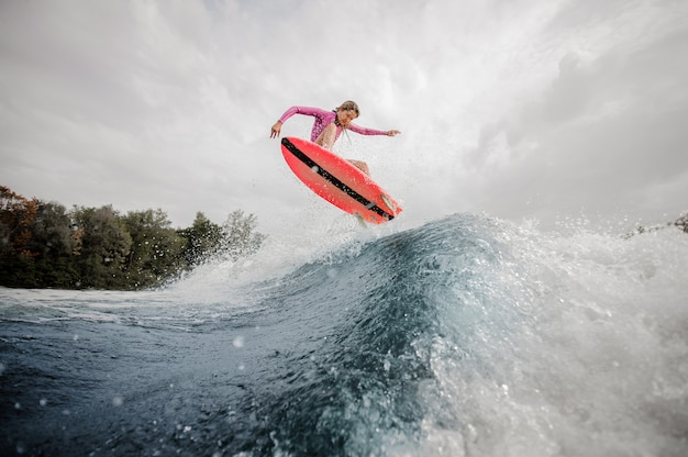 Surfeur femme blonde sautant la vague d'éclaboussures bleues contre le ciel