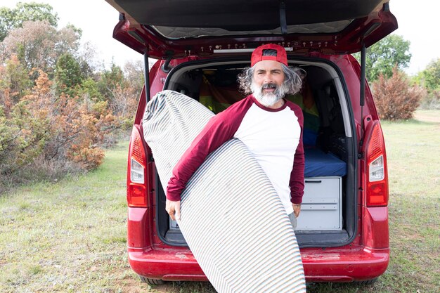 Surfeur hipster attrayant regardant la caméra tenant une planche style de vie d'aventure sportive en plein air