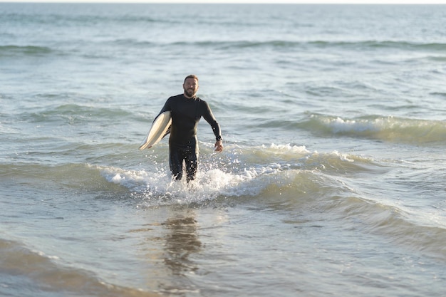 Surfeur homme souriant sortant de la mer tenant une planche de surf