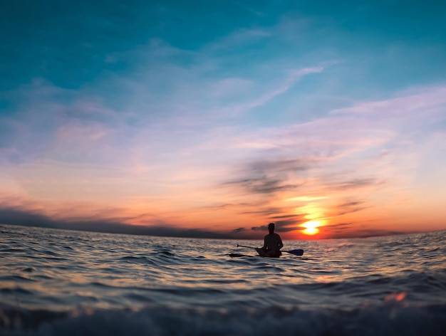 Un surfeur pagaie dans l'eau au coucher du soleil.