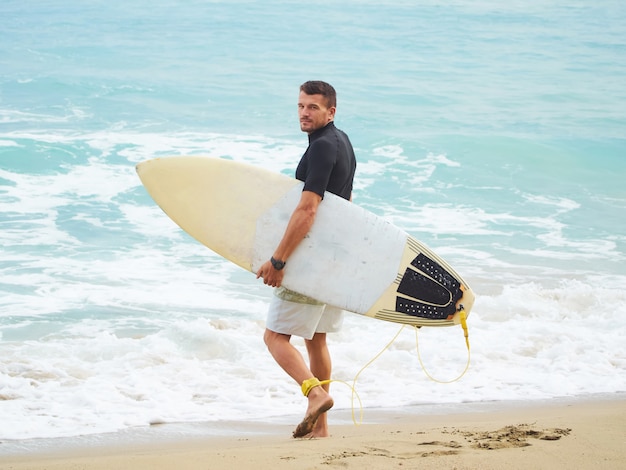 Le surfeur avec une planche de surf se rend dans l'océan. Habillé en short et lycra. Plage sur l'océan Atlantique.