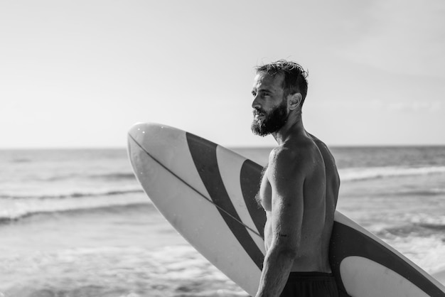 Surfeur tenant sa planche de surf sur la plage Homme hipster debout sur la plage et attendant de grosses vagues pour surfer Fit homme barbu s'entraînant avec planche de surf à la mer Concept de style de vie et de liberté