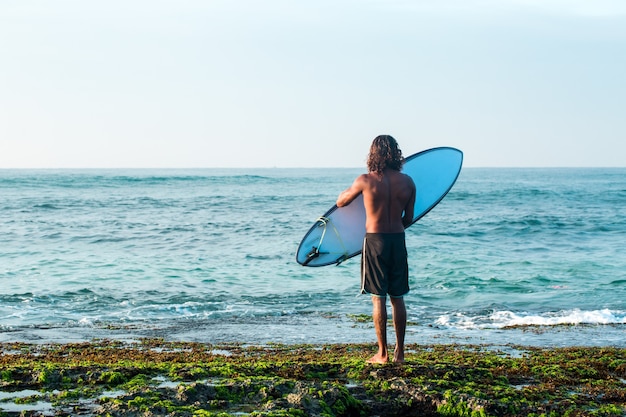 Le surfeur tient une planche de surf sur la rive de l'océan Indien