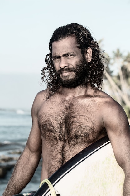 Le surfeur tient une planche de surf sur la rive de l'océan Indien