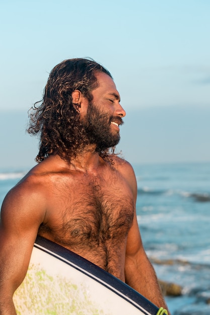 Le surfeur tient une planche de surf sur la rive de l'océan Indien