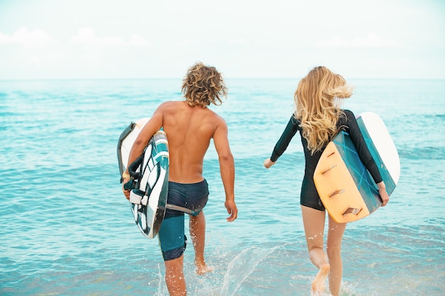 Surfeurs à la plage - Couple souriant de surfeurs marchant sur la plage et s'amusant en été