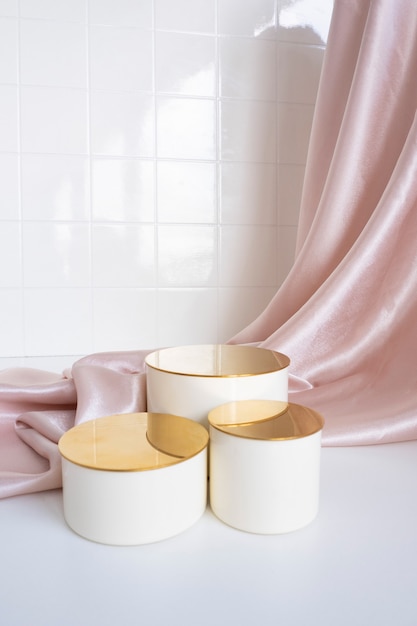 Surmatelas trois podiums beiges avec un dessus doré sur fond satiné à plis. carrelage de fond dans la salle de bain.