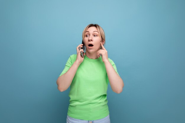 Surpris adorable femme blonde parlant au téléphone sur un fond bleu avec copie espace