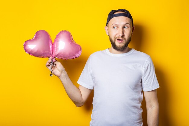 Surpris choqué jeune homme barbu tenant des ballons à air coeur rose