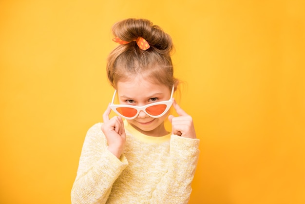 Surpris drôle de petite fille à lunettes de soleil sur mur jaune