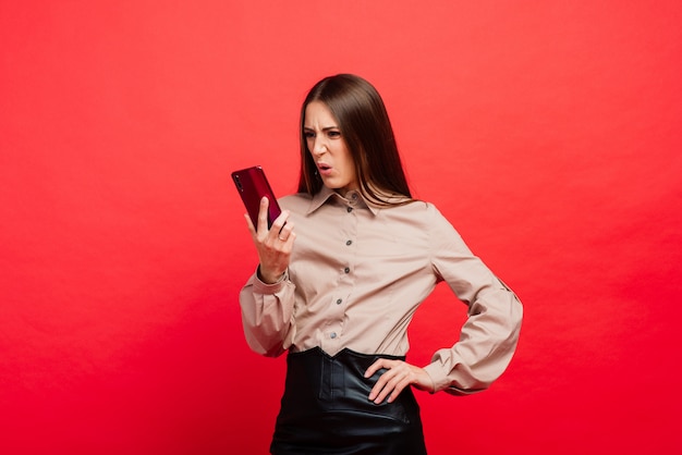 Surpris de jeune femme à l'aide de smartphone sur fond rouge