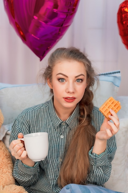 Surpris jeune femme aux cheveux longs prend son petit déjeuner au lit le jour de la Saint-Valentin