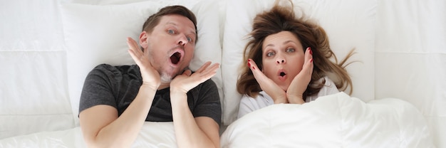 Surpris jeune femme et homme allongé dans le lit vue de dessus confortable concept de matelas orthopédiques