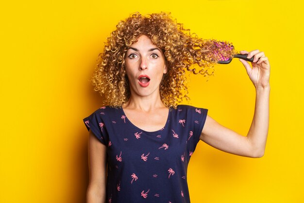 Photo surpris jeune femme peignant les cheveux bouclés emmêlés sur fond jaune.