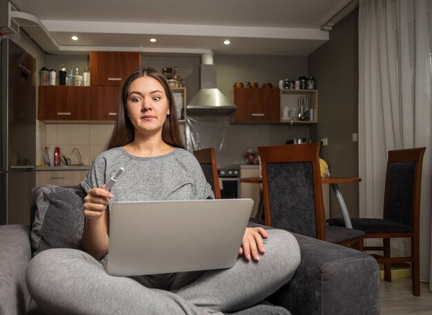 Surpris jeune femme et test de grossesse avec ordinateur portable, femme à la recherche d'informations sur la grossesse sur Internet avec ordinateur portable